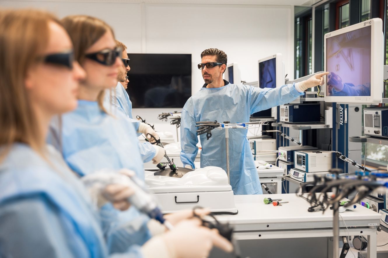 Medizinische Schulung mit Teilnehmenden in blauen Kitteln, die chirurgische Instrumente und Monitore in einem Hightech-Labor verwenden