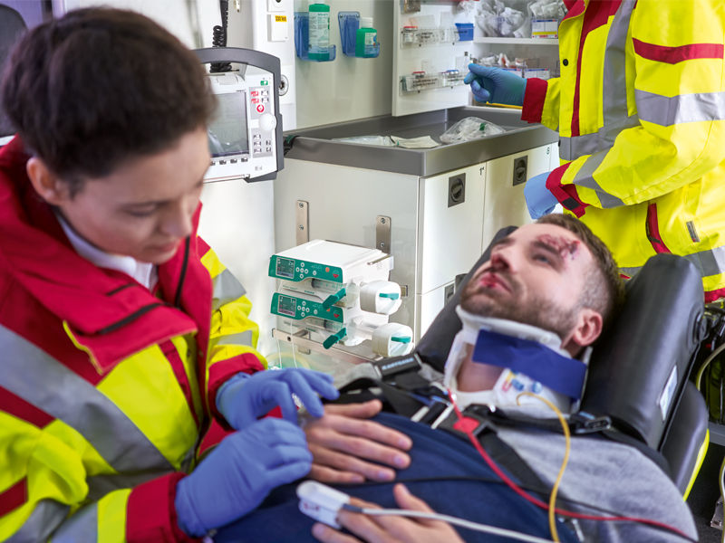 Eine medizinische Fachkraft führt in einem Krankenwagen mit medizinischen Pumpen Erste Hilfe bei einem Mann mit Blut im Gesicht durch