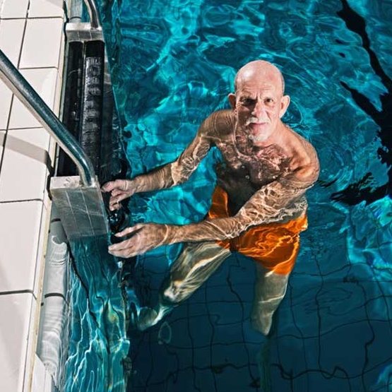 Ein älterer Mann steht an einer Leiter im Schwimmbad